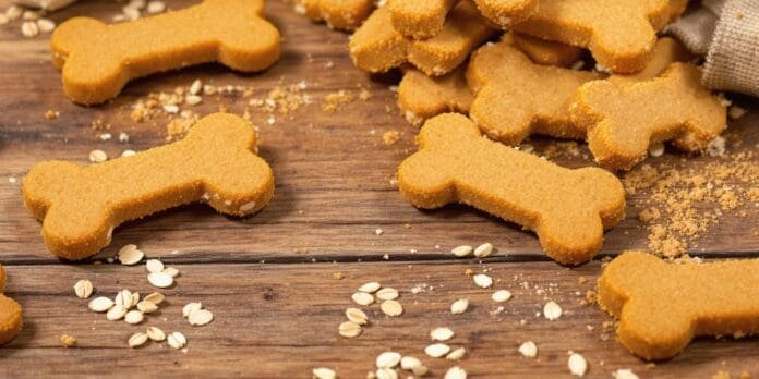 Artisan dog biscuits on a wooden surface with ingredients.