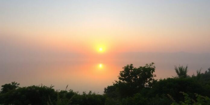 Tranquil sunrise over a calm lake with greenery.